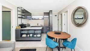 A modern kitchen with a central island, a dining area with a round table and blue chairs, and a large mirror on the wall. - The Emerald 42 (Sandton)