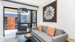 A modern living room with a grey sofa, orange cushions, a black coffee table with a gold bowl, and a large abstract flower painting on the wall. - The Emerald 42 (Sandton)
