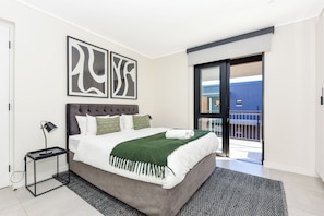 Relax in this serene hotel room featuring a large bed, a black nightstand, and a sliding glass door leading to a balcony.
