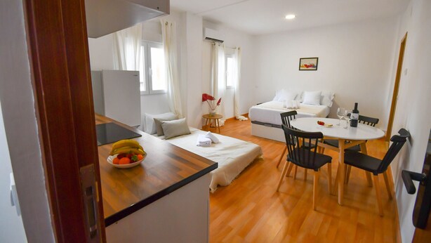 A modern hotel room with a wooden floor, a bed with white bedding, a dining table with chairs, and a small table with a bowl of fruit. - APARTAMENTO TETUAN "CASTELLANA" (Madrid)