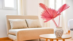 A modern living room with a beige sofa, a small round wooden table, and a vase with red paper fans. - APARTAMENTO TETUAN "CASTELLANA" (Madrid)
