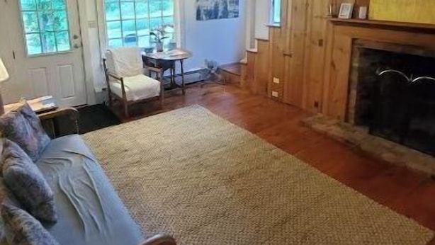 Een ruime woonkamer met een groot vloerkleed, houten balken, een open haard en een eethoek met een tafel en stoelen.