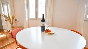 Ett runt, vitt bord med en vinflaska och ett glas, en tallrik med jordgubbar och en vas med torkade växter.