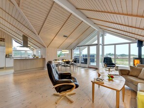 A spacious living area with a high ceiling and large windows, a kitchen with a central island, and a cozy seating area with a fireplace.