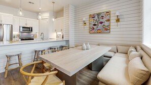 Une cuisine moderne avec des meubles blancs, une table à manger en bois et un banc intégré doté de coussins.