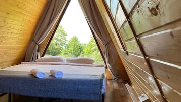 A cozy room with a sloped ceiling, a bed with pillows, a window, and a wooden floor.