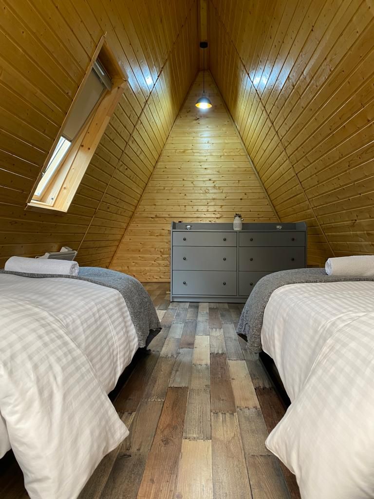 Una habitación con dos camas, un aparador y techo inclinado.