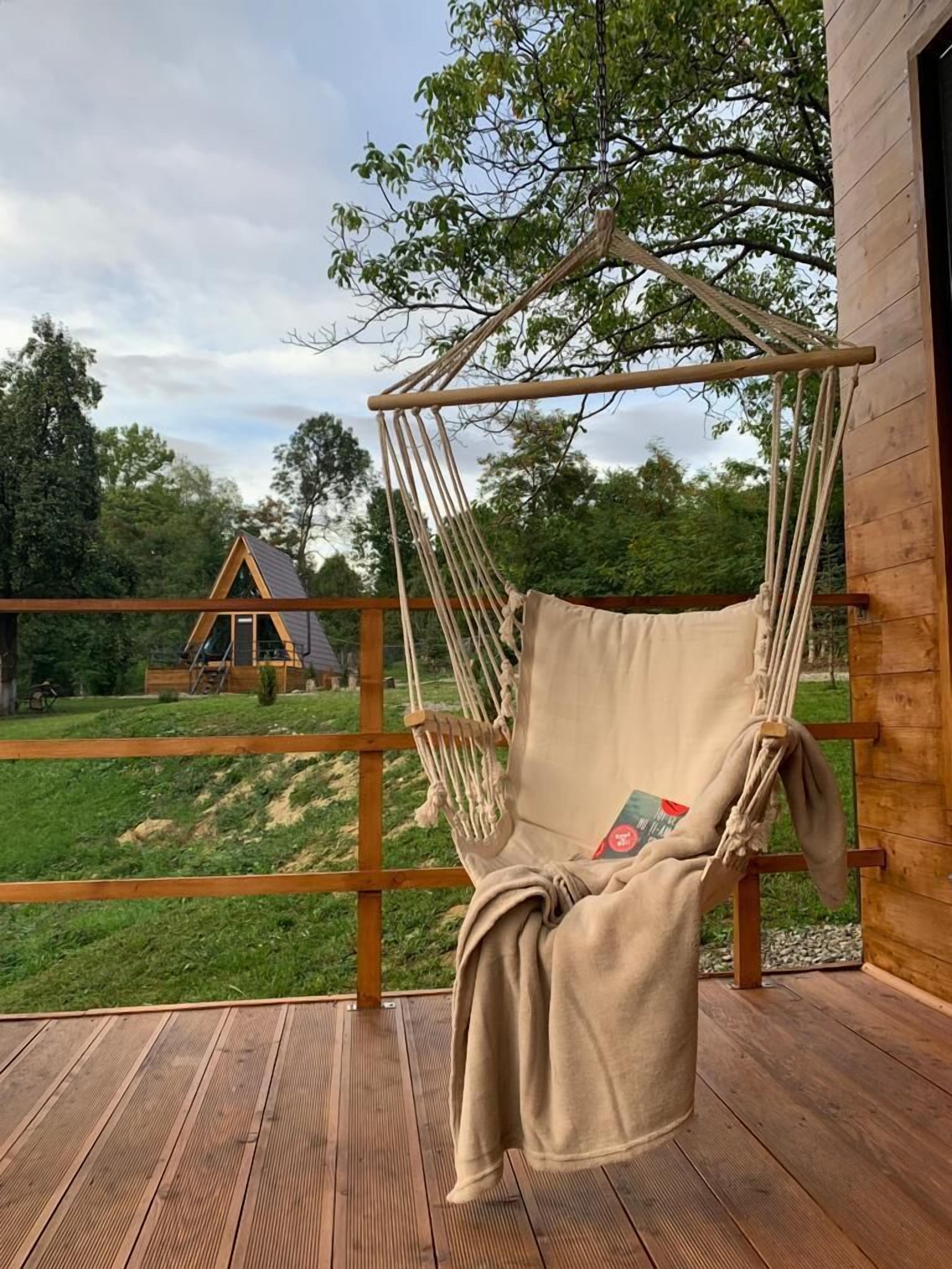 A wooden deck with a hanging chair and a view of a house in the background.