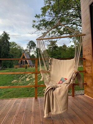 Une terrasse en bois avec un fauteuil suspendu et, au loin, une maison en arrière-plan.