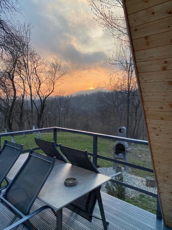 An outdoor deck with a table and chairs, overlooking a forested landscape with a sunset. - Casutele din Poienita Chalet (Comarnic)