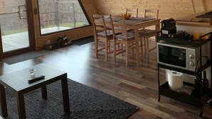 Una habitación acogedora y bien iluminada, con techo de madera, una mesa de comedor con sillas, una zona de cocina con microondas y un amplio ventanal con vistas al exterior.