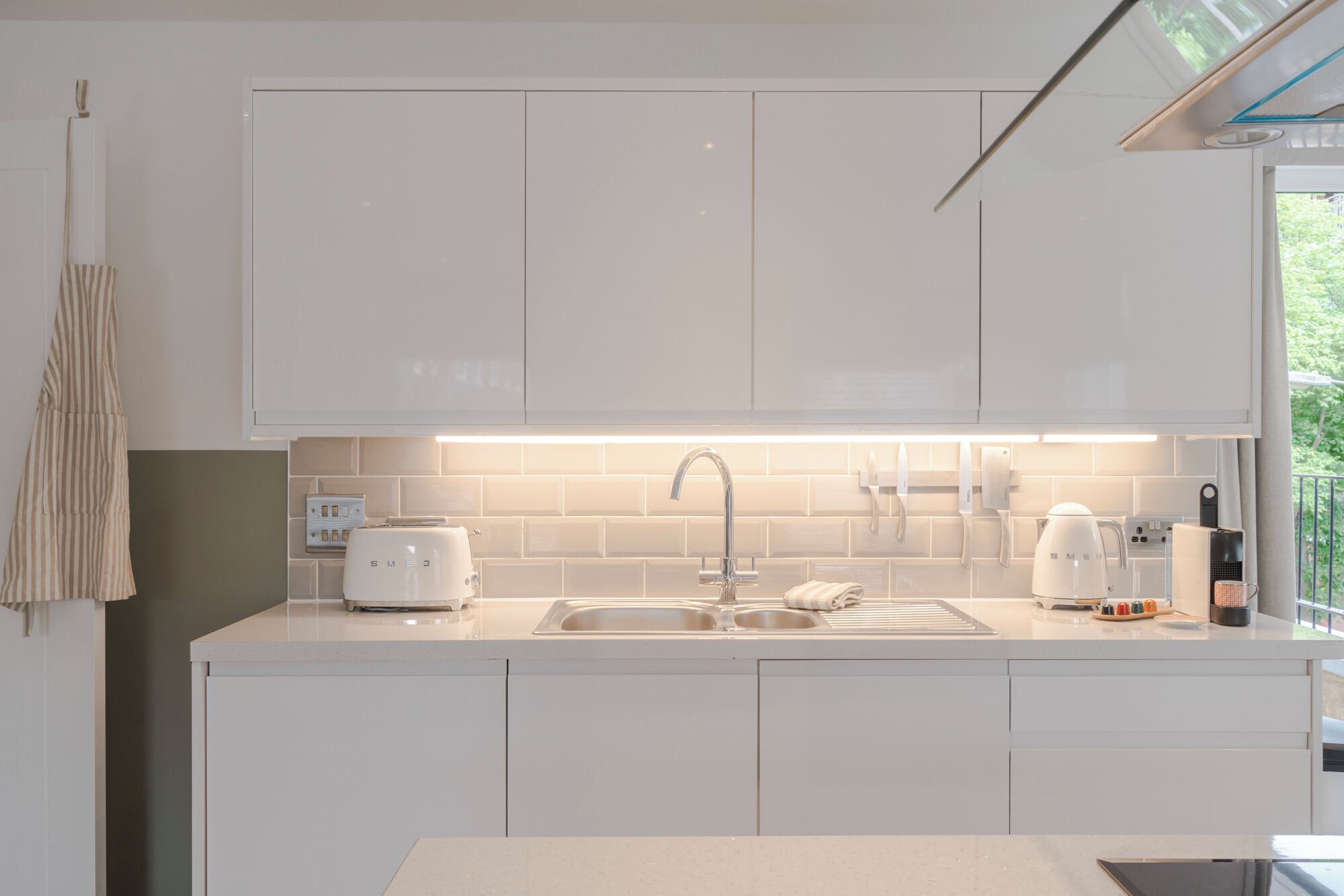 A modern kitchen with white cabinets, a stainless steel sink, and a built-in toaster.