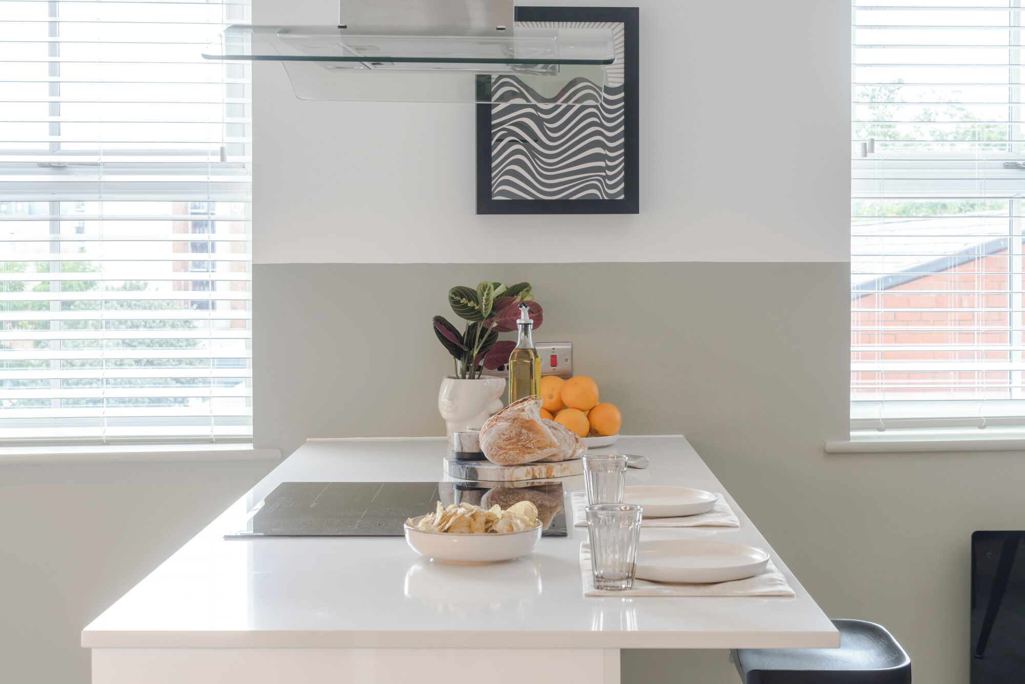 A modern kitchen with a central island, a potted plant, a bottle, and oranges on the counter.