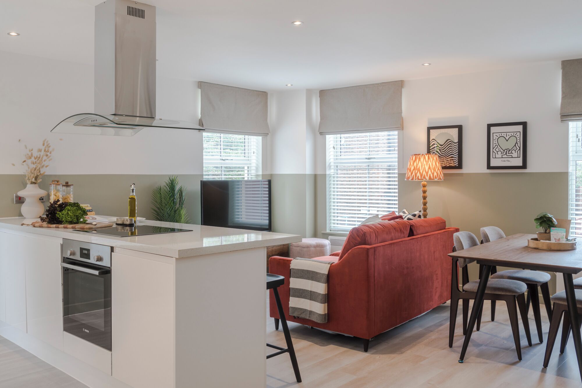 Une cuisine moderne avec un îlot central, un coin repas avec un canapé et des fauteuils rouges, et une table à manger.
