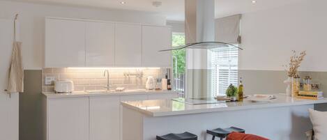 A modern kitchen with white cabinetry, a central island with stools, and a red sofa in the adjacent living area.