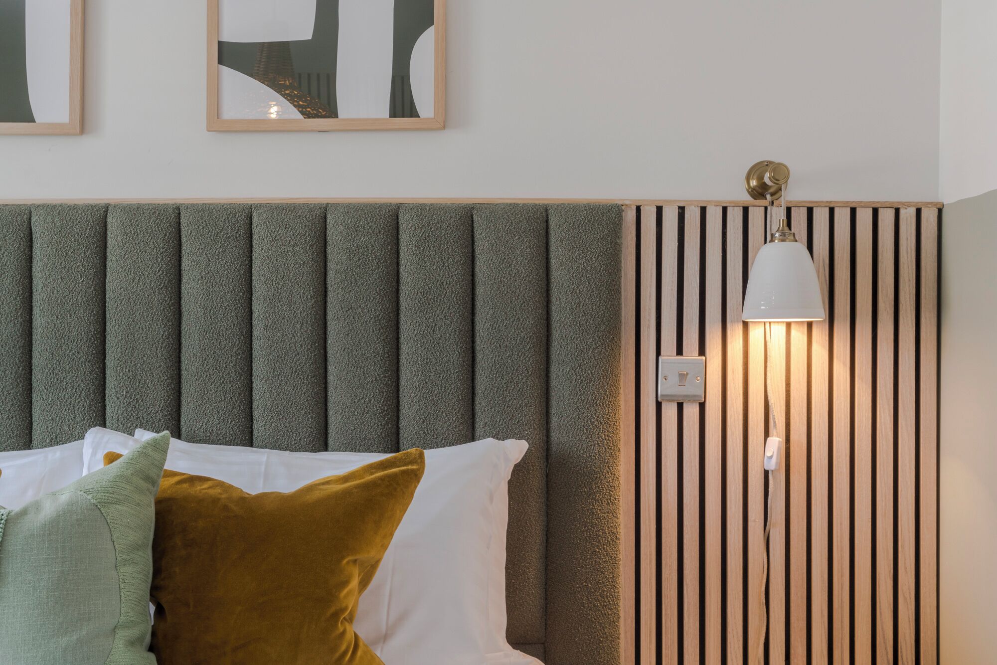 Una camera da letto con un letto, cuscini, una lampada a parete e una testiera decorata.