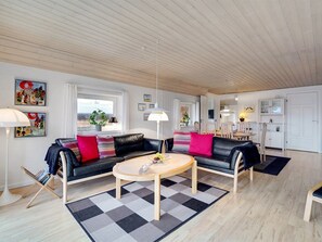 A modern living room with a black leather sofa, a round coffee table, and a checkered rug. There is a dining area in the background with a white cabinet and a hanging light fixture.