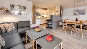 Una sala de estar moderna con un sofá, una mesa de comedor con sillas, una zona de cocina y una pequeña isla con un fregadero.