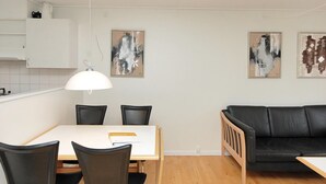 A modern living room with a dining area, featuring a black leather sofa, a white dining table with four chairs, and two abstract paintings on the wall. - "Enni" - 100m from the sea by Interhome (Hals)