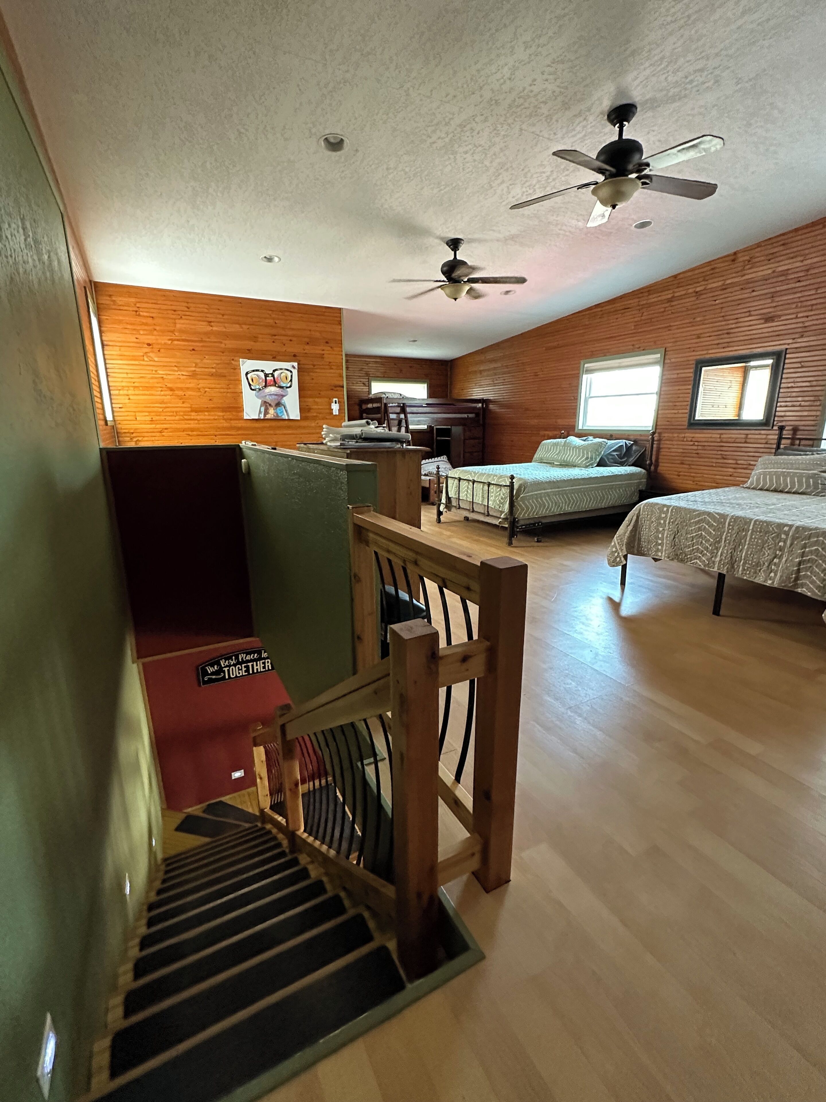 A spacious room with a wooden floor, a bunk bed, a desk, and a ceiling fan.
