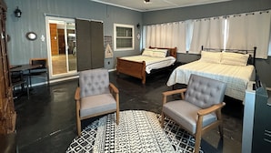 Un dormitorio con dos camas, ventilador de techo, alfombra estampada y un área de descanso con sillas.