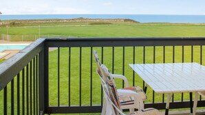 A balcony with a view of a grassy field and the sea.