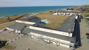 A coastal building with a swimming pool, parking area, and a view of the sea.