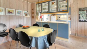 Een moderne keuken met houten lambrisering, een centraal kookeiland met spoelbak, en een eethoek met een ronde tafel en stoelen.