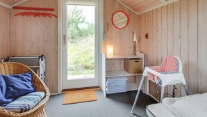 Een gezellige kamer met houten inrichting, een rieten stoel, een klein tafeltje met een kussen met rode strepen en uitzicht door een glazen deur.