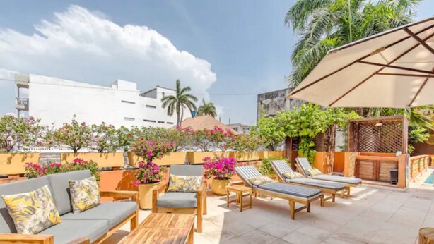 Un patio al aire libre con mobiliario de madera, un espacio de descanso y plantas en macetas.