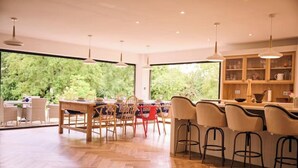 A spacious kitchen with a large island, wooden flooring, and a view of greenery through the windows. - Stunning new Build by the River (Costessey)