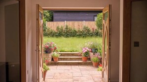 A doorway leading to a garden with a wooden fence, potted plants, and a grassy lawn. - Stunning new Build by the River (Costessey)