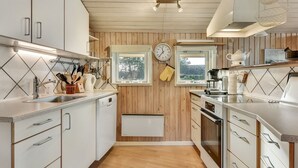 A modern kitchen with wooden paneling, white cabinets, stainless steel appliances, and a window providing natural light. - "Hjalmar" - 400m from the sea by Interhome (Millinge)