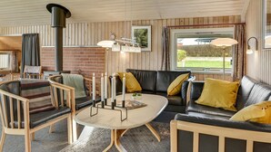 A cozy living room with a fireplace, wooden furniture, and a large window offering a view of the outdoors. - "Hjalmar" - 400m from the sea by Interhome (Millinge)
