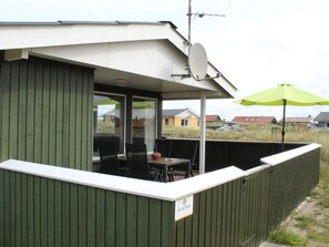 Ett takförsett utomhusområde med bord och stolar, ett grönt parasoll och en skylt som visar platsen.