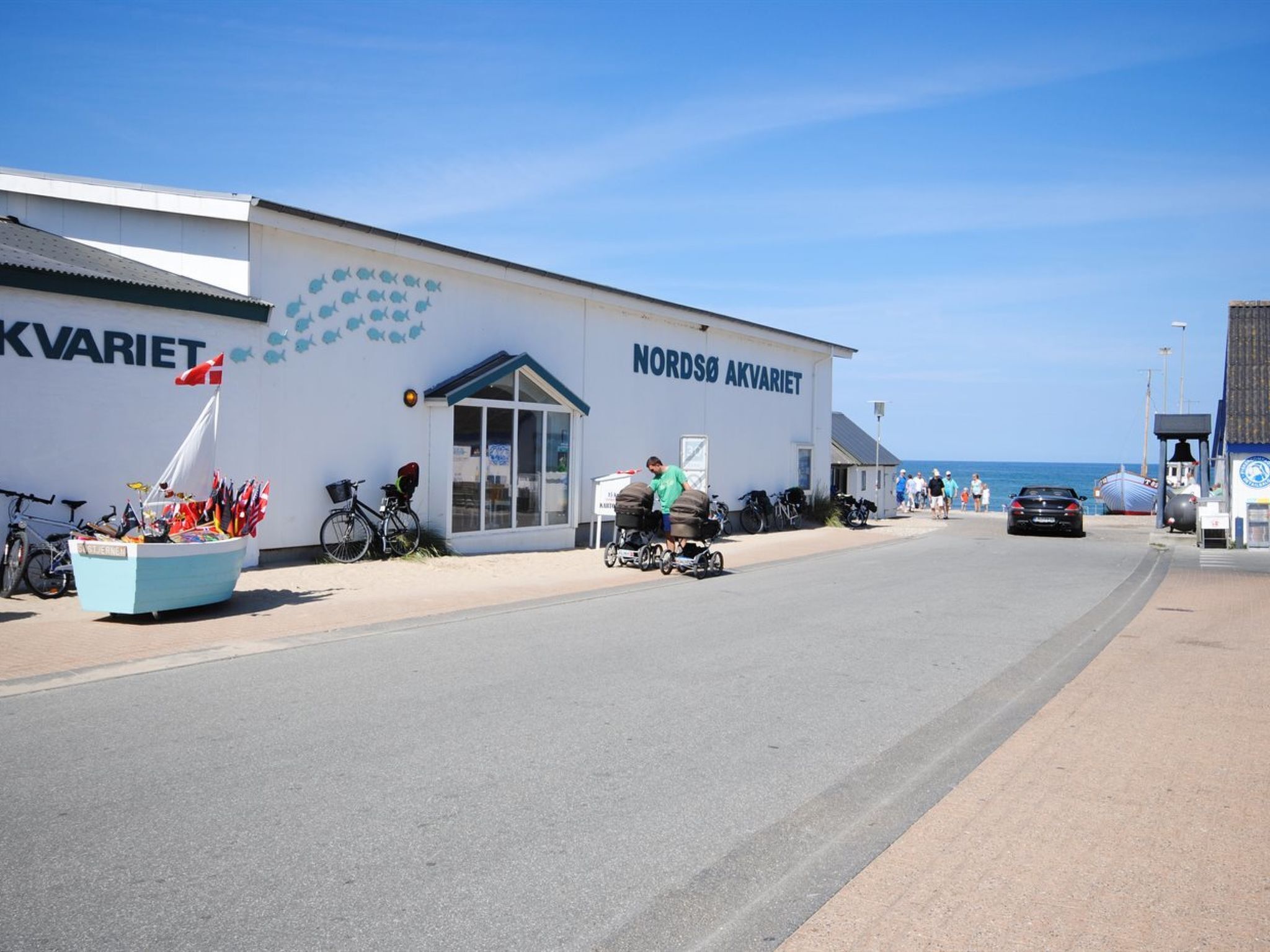 Un bâtiment sur lequel on peut lire l’inscription « NORDSØ AKVARIET », et un petit bateau décoré de drapeaux, devant l’entrée.