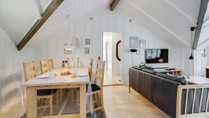 Un vaste espace de vie doté d’un haut plafond, d’une table à manger en bois et d’un coin salon confortable avec un canapé et un téléviseur.