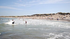 Une plage où l’on peut faire du surf et de la baignade, avec des dunes de sable en arrière-plan et un ciel dégagé.