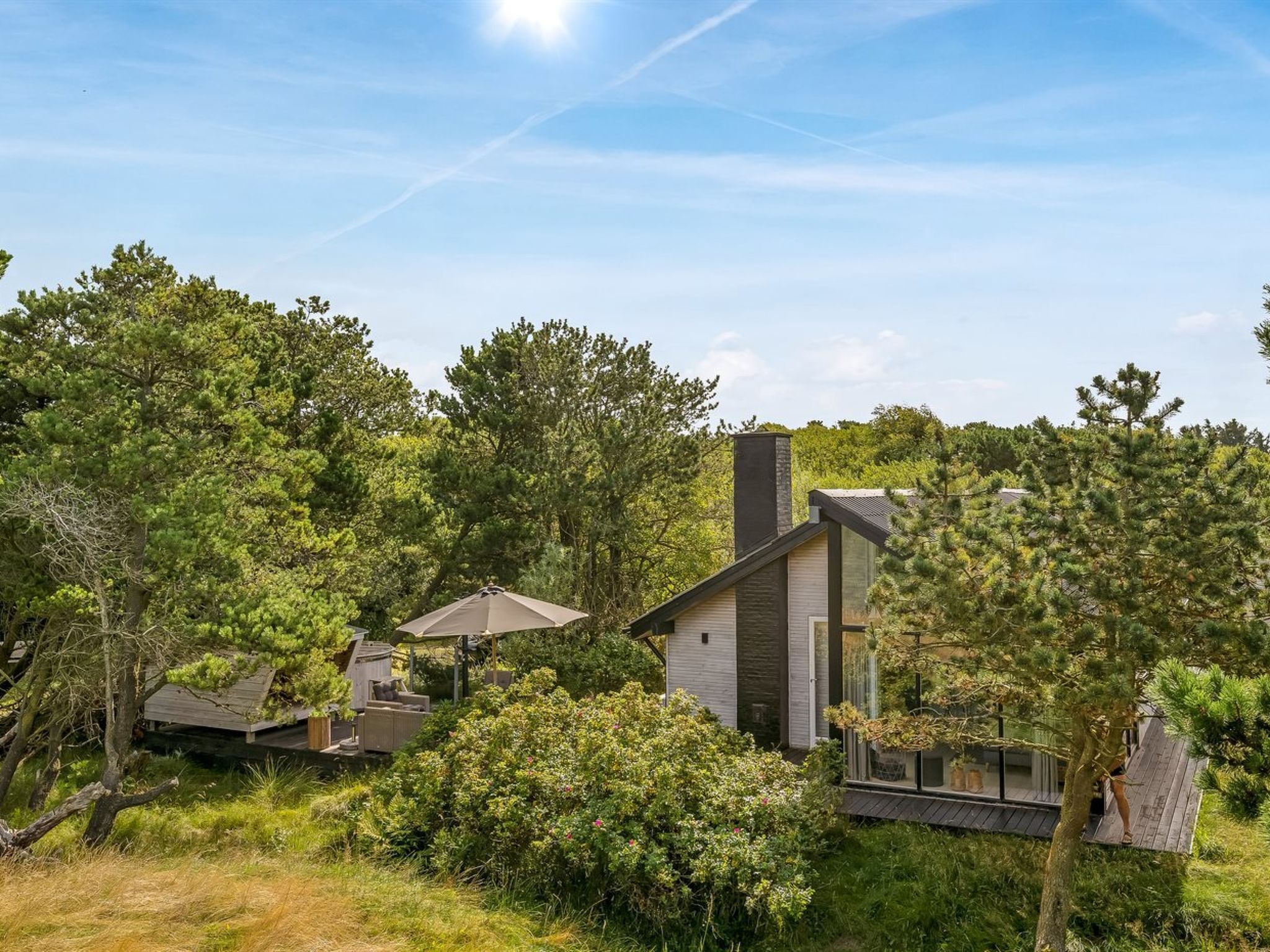 Une maison moderne dotée d’une grande cheminée, entourée d’arbres denses et surplombant un ciel dégagé.