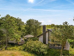 Een modern huis met een grote schoorsteen, omgeven door dichte bomen en een heldere lucht.