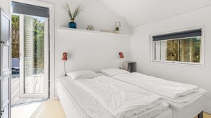 Een slaapkamer met een bed, een raam, een deur en een plank met planten.