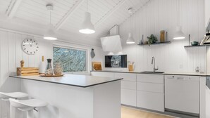 Een moderne keuken met witte kasten, een centraal eiland, hanglampen en een raam met uitzicht op bomen.
