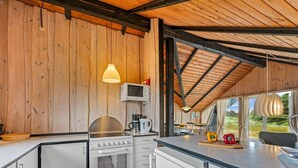 A modern kitchen with wooden walls, a built-in oven, a microwave, and a dining area with a view. - "Hildegart" -  from the sea by Interhome (Hvide Sande)