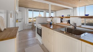 A modern kitchen with wooden ceiling beams, white cabinetry, and a large window offering a view of the countryside. - "Vina" - 200m to the fjord by Interhome (Hvide Sande)