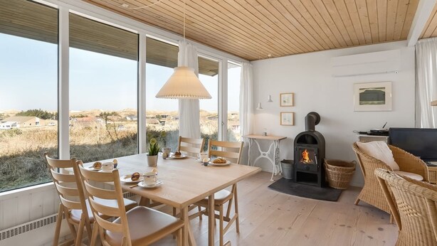 A cozy room with a wooden table and chairs, a fireplace, and large windows offering a view of the countryside. - "Vina" - 200m to the fjord by Interhome (Hvide Sande)