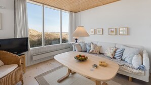 A cozy living room with a large window, a television, a sofa with cushions, a table with a bowl of fruit, and a lamp. - "Vina" - 200m to the fjord by Interhome (Hvide Sande)