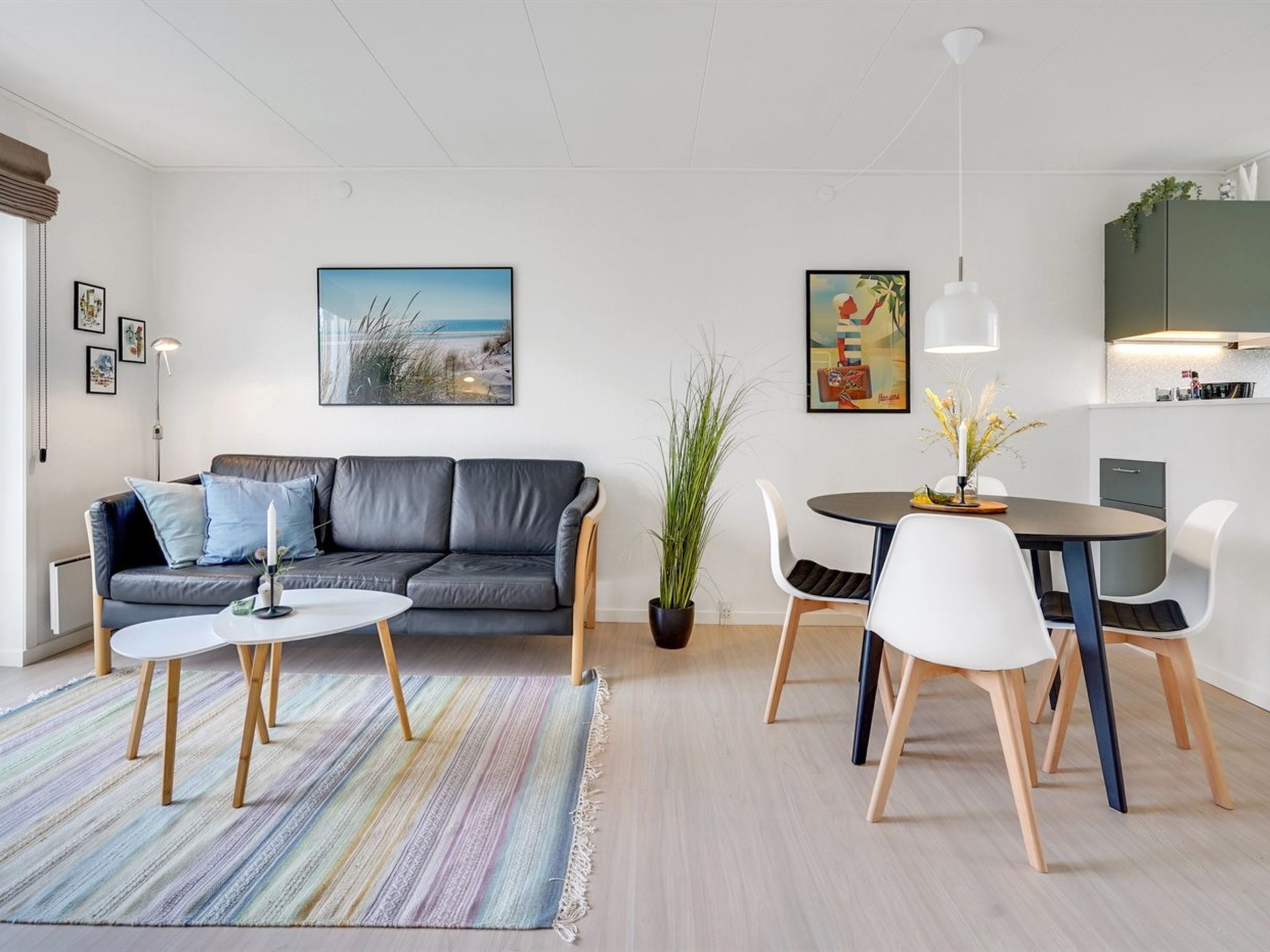 A modern living room with a grey leather sofa, a round dining table with white chairs, and a colorful striped rug.