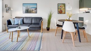 A modern living room with a grey leather sofa, a round dining table with white chairs, and a colorful striped rug. - "Sipi" - 100m from the sea by Interhome (Hals)