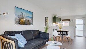 A modern living room with a black leather sofa, a small white table, and a colorful striped rug. There is a dining area with a white table and chairs, and a kitchen in the background. - "Sipi" - 100m from the sea by Interhome (Hals)