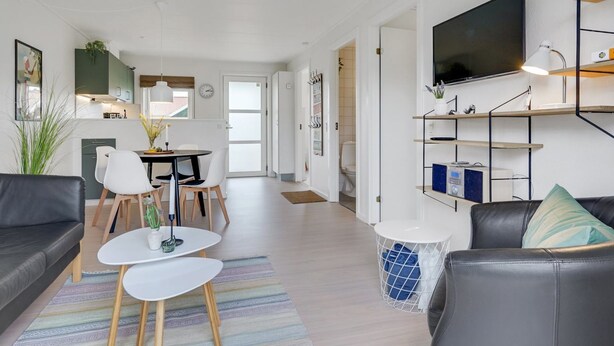 A modern living room with a black leather sofa, a white coffee table, and a TV mounted on a wooden shelf. - "Sipi" - 100m from the sea by Interhome (Hals)